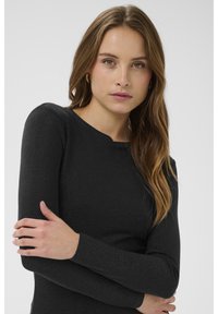 Hosszú ujjú fekete felső texturált, csillogó anyagból, lekerekített nyakkivágással, testhezálló ujjak és finom dizájn jellemzi.