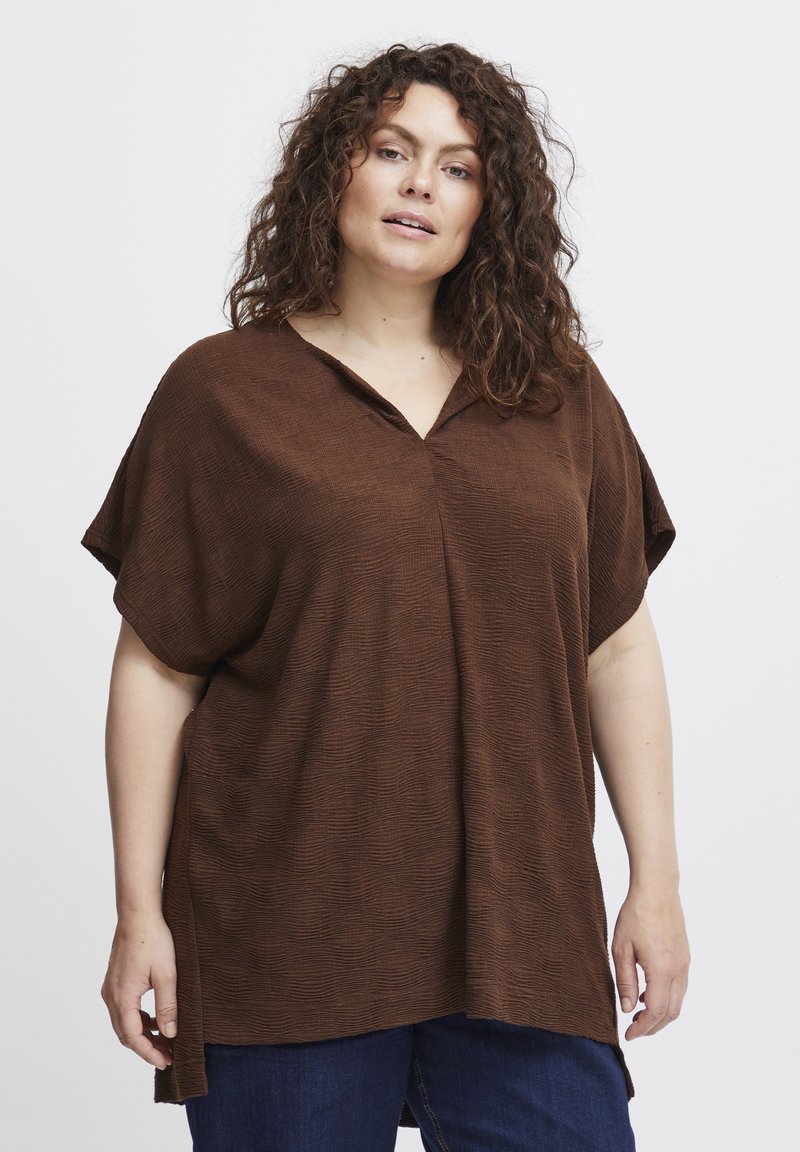 Brun oversized top med et tekstureret mønster, V-hals og korte ærmer. Kombineret med mørkeblå denimjeans.