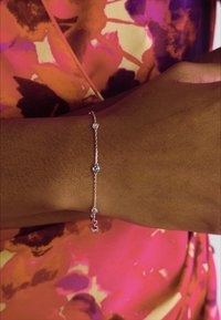 Bracciale d'argento con quattro accenti circolari, caratterizzato da una delicata catena e una superficie lucida, indossato su un polso marrone.