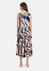 Ärmelloses Midikleid mit einem gestuften Design, das ein welliges blaues, beiges und weißes abstraktes Muster auf leichtem Stoff zeigt. Detail mit Schlüsselloch hinten.