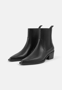 Bottines noires en cuir avec des pointes aiguës. Panneaux latéraux élastiques et languettes de traction. Talons carrés avec une texture lisse et des détails de design minimalistes.