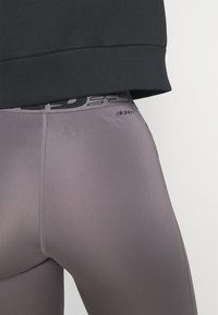 Szare legginsy sportowe o gładkiej, elastycznej fakturze. Posiadają czarną talię z logo oraz subtelne detale szwów. Odpowiednie do aktywności.