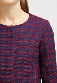 Navy and red patterned dress with a round neckline. Textured fabric features a geometric design and contrasting color accents.