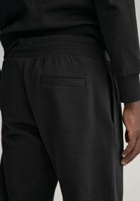 Czarne dresy z fakturowanej tkaniny, z boczną kieszenią i prostą tylną kieszenią. Elastyczny pas z uszczelnieniem z prążków.