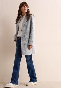 Ljust grå, strukturerad kappa med notched krage och två framfickor, kombinerad med blå utsvängda jeans och vita sneakers.