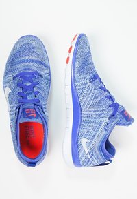 Zapatillas de correr Nike Free 5.0 en material de punto azul claro con acentos en azul oscuro, con un swoosh blanco y un logo rojo en la plantilla.