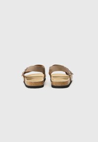 Sandale din piele marron cu două curele reglabile, talpă din plută și talpă din cauciuc negru, având o suprafață texturată și un design minimalist.