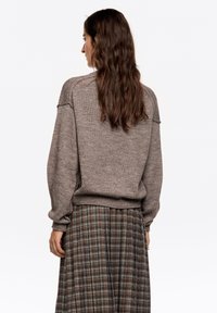 Brązowy dziergany sweter o luźnym kroju z prążkowanymi mankietami, zestawiony z długą, kraciastą spódnicą w ziemistych odcieniach o rozkloszowanym kroju.