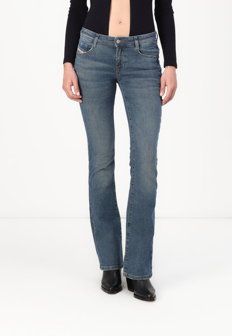 Faded blue denim jeans, flared leg design, standard five-pocket style, stitched detailing on pockets, worn with black heeled boots.