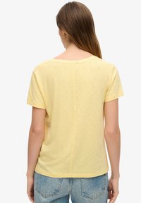 Geel T-shirt met korte mouwen, gemaakt van lichtgewicht stof, met een ronde halslijn en een naaddetail dat langs de achterkant loopt.