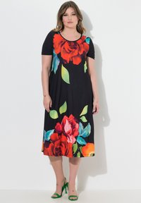 Czarna sukienka z krótkim rękawem, z dużymi czerwono-niebieskimi kwiatowymi wzorami, o długości do kolan, wykonana z miękkiego materiału o luźnym kroju. Dopełniona zielonymi sandałami.