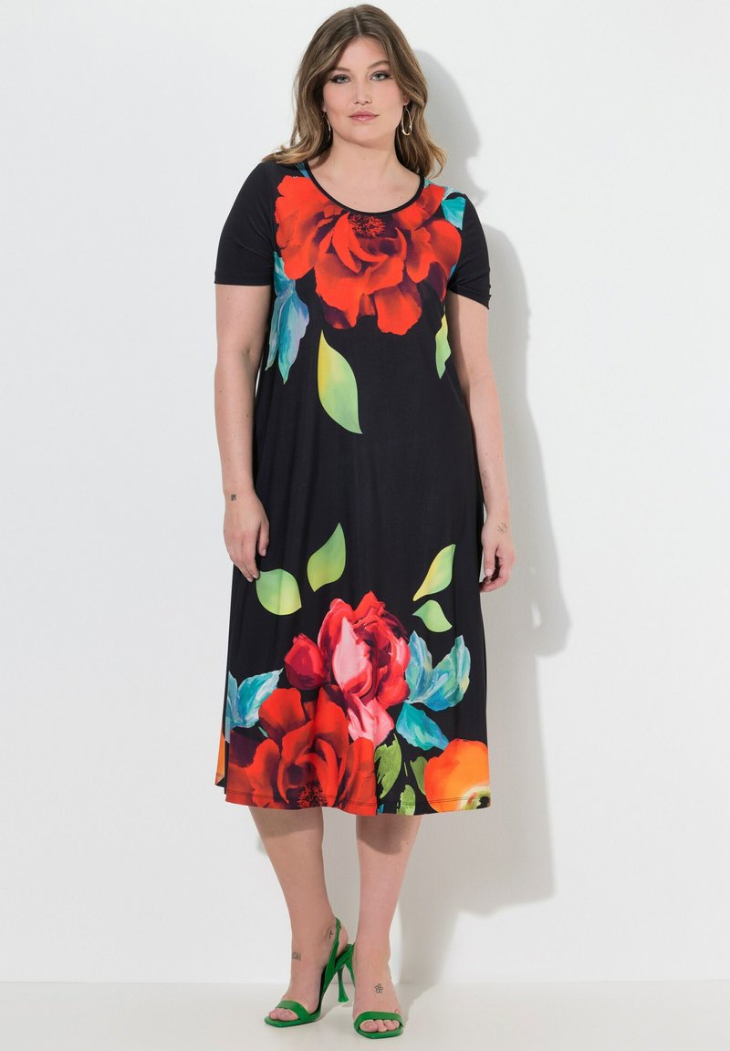 Czarna sukienka z krótkim rękawem, z dużymi czerwono-niebieskimi kwiatowymi wzorami, o długości do kolan, wykonana z miękkiego materiału o luźnym kroju. Dopełniona zielonymi sandałami.