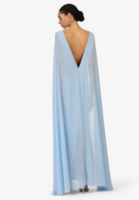 Robe cape bleu clair présentant un dos en V profond, un tissu transparent flottant et un design minimaliste avec un drapé élégant.