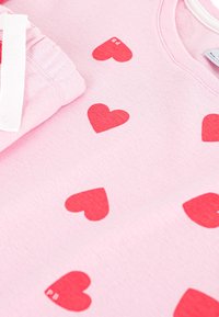 Felpa rosa chiaro con stampa di cuori rossi sparsi, con collo a costine e texture morbida. Piegata ordinatamente con dettagli dell'etichetta bianca.