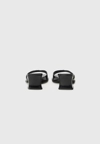 Sandalias de charol negras con un respaldo abierto cuadrado, que cuentan con un tacón ancho y un diseño minimalista. Textura suave y apariencia elegante.