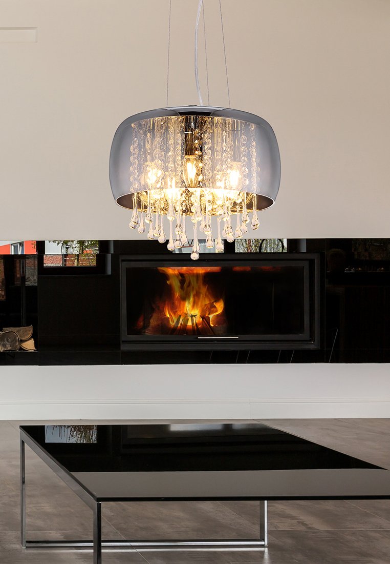 Moderne Deckenleuchte mit hängenden Kristallen über einem schwarzen Glastisch und einem beleuchteten Kamin in einem minimalistischen Wohnzimmer.