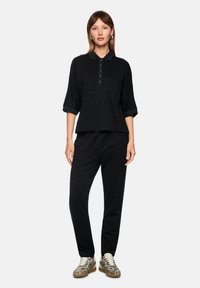 Schwarzes, strukturiertes Oberteil mit Kragen und Knöpfen, kombiniert mit passenden schwarzen Hosen. Das Outfit zeichnet sich durch ein dezentes Zebramuster und eine lockere Passform aus.