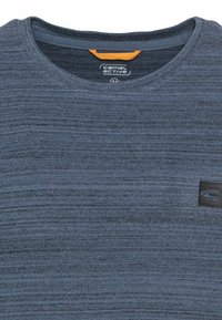 Blå struktureret crew-neck t-shirt lavet af blødt stof, med et sort logo-lap på brystet og en orange detalje ved halsen.