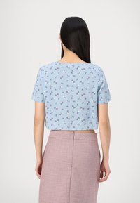 Top corto de manga corta en tejido azul claro con un patrón floral en morado y blanco. Combinado con una falda texturizada rosa.