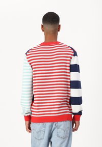 Pull rayé multicolore comprenant du rouge, bleu clair, bleu marine et blanc. Texture tricotée avec poignets et ourlet côtelés. Coupe décontractée.