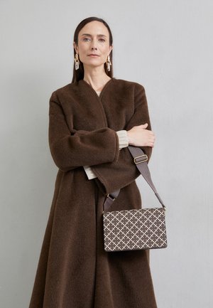Cappotto marrone peloso con maniche ampie, top in maglia color crema e borsa rettangolare a motivo geometrico in beige e marrone.