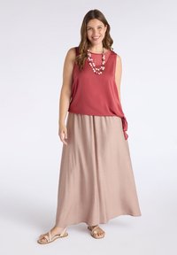 Top senza maniche color ruggine con un nodo laterale, abbinato a una maxi gonna beige chiaro. Accessoriato con una collana di perle multicolori e sandali.