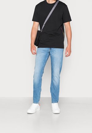 Black short-sleeve t-shirt, light blue denim jeans, and white sneakers. A black bag with a gray strap is worn across the body.