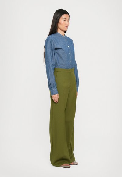 Camicia in denim con colletto, abbinata a pantaloni verdi oliva a vita alta e a gamba larga. Il modello indossa scarpe slip-on a righe.