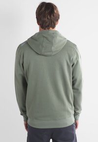 Sweatshirt à capuche vert olive avec une coupe décontractée, présentant des détails de couture visibles, des poignets côtelés et une poche kangourou.