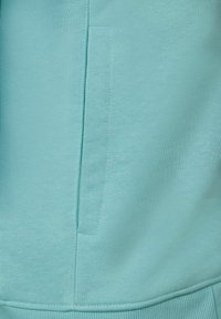 Light blue sweatshirt in soft cotton blend, featuring a side pocket and ribbed hem. Texture appears smooth with a subtle stretch.