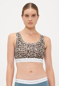 Kvinde iført en sports-bh med leopardmønster og blå høj talje leggings med hvide elastiske bånd, der er mærket "Copenhagen Studios."