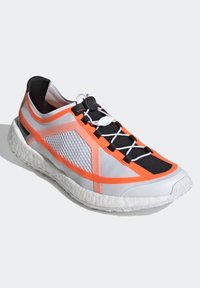 Scarpa sportiva con lacci, in mesh grigio e nero, con accenti arancioni brillanti e suola bianca texturizzata. Presenta un sistema di allacciatura sicura.