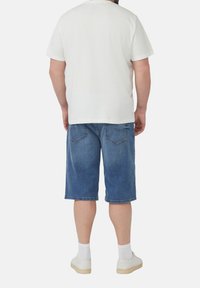 Weißes T-Shirt mit kurzen Ärmeln, blaue Jeansshorts und weiße Sneakers mit sichtbaren gestreiften Socken; schlichtes Design, lockere Passform, keine auffälligen Muster.