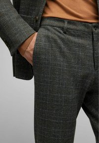 Gevlekte broek in donkergrijs met oranje accenten, gemaakt van textuurstof. Heeft een platte voorkant en zijzakken, gecombineerd met een bruine trui.