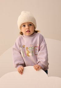 Felpa viola chiaro con design grafico colorato che raffigura animali e stelle. Cuffia lavorata a maglia color crema, acconciatura a coda di cavallo e sfondo neutro.