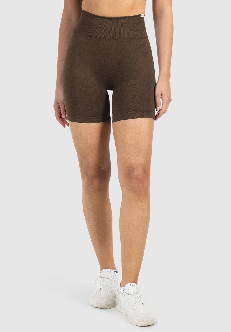 Hooggewaiste bruine shorts gemaakt van rekbaar materiaal, met een gladde textuur en een strakke pasvorm, gecombineerd met witte sportieve sneakers.