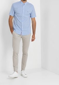 Camicetta a maniche corte in Gingham blu con colletto abbottonato, abbinata a pantaloni slim-fit beige e sneakers bianche. Look pulito e casual.