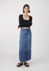 Crni dugosleeve top s nabranom teksturom, uparen s traper maxi suknjom visokog struka koja ima prednji izrez. Crne japanke.