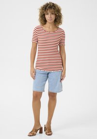 Gestreepte rood en room ribbel top met een gekrulde halslijn en mouwen. Gecombineerd met lichtblauwe denim shorts en bruin hoge sandalen.