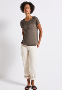 Olive green short-sleeve top with a textured yoke, paired with cream pants, rolled at the cuffs, and black slip-on sandals.