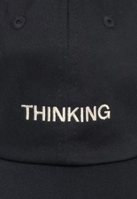Casquette noire à visière incurvée, ornée d'un texte brodé blanc "PENSER" à l'avant. Le texte est centré et en gras sur la texture du tissu.