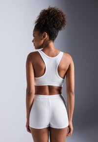 Hvit ribbet sports-bh med brede stropper, kombinert med matchende shorts. Stoffet ser elastisk ut, designet for komfort og bevegelighet, sømløse detaljer.