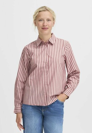 Camicia a righe rosa e bianca, con colletto e maniche lunghe. Realizzata in tessuto leggero, abbinata a jeans in denim blu.