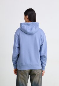 Light blue hooded sweatshirt featuring a relaxed fit, ribbed cuffs, and hem, with a soft texture visible on the fabric surface.