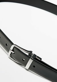 Svart läderbälte med en glänsande silvermetallspänne, har en slät yta och flera hål för justerbarhet.