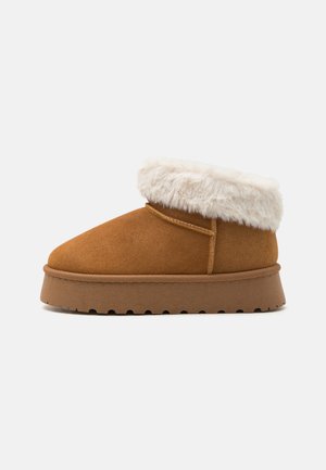 Brown suede ankle boot with a white faux fur cuff, round toe, and textured rubber sole featuring a wave pattern. Minimalistic design.