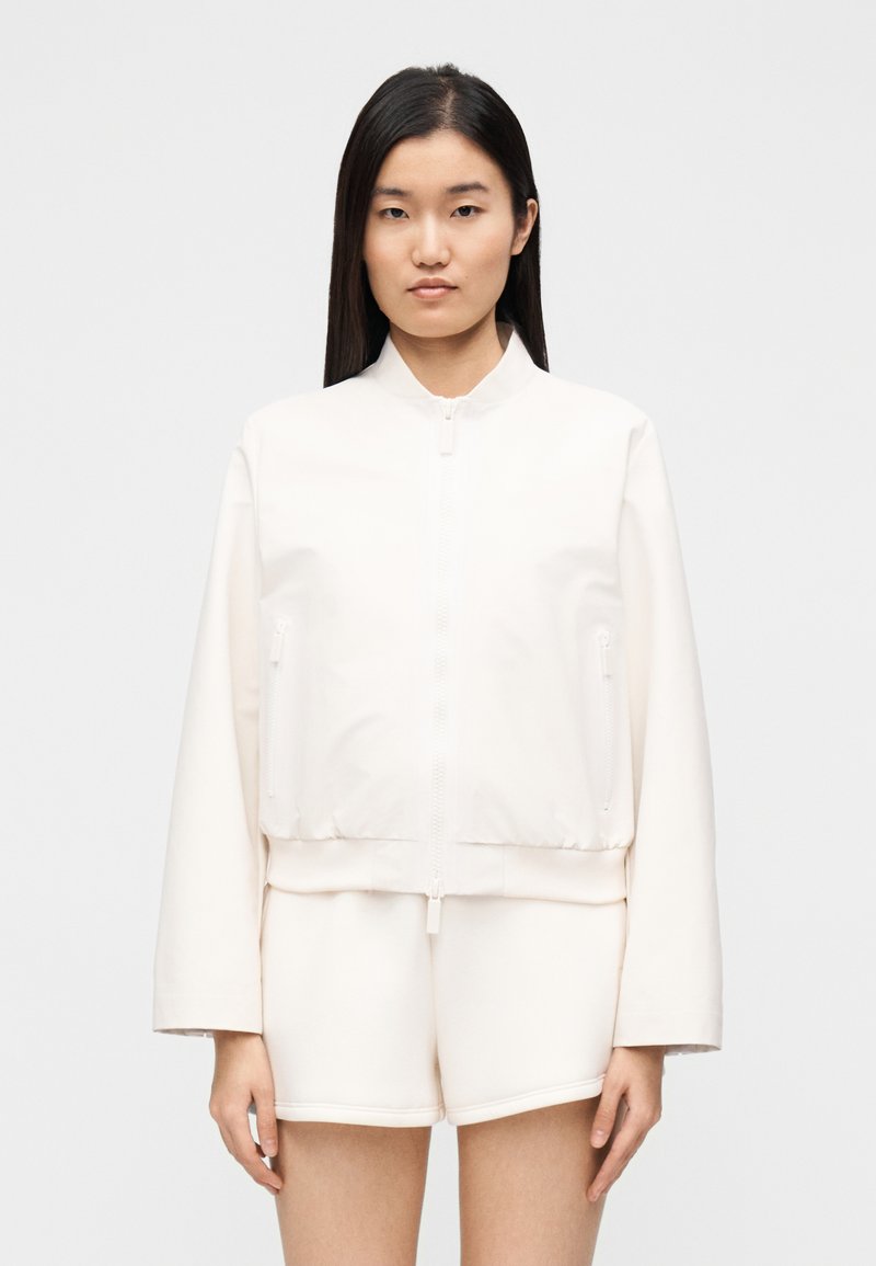 Ελαφρύ κρεμ μπόμπερ μπουφάν με φερμουάρ στο εμπρός μέρος, ριμπ τελείωμα και δύο πλαϊνές τσέπες. Διαθέτει απλό σχέδιο και λεία υφή.