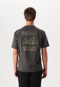 Camiseta de algodón de color gris oscuro con un gran gráfico en la parte posterior que incluye el texto "DICKIES" y "HIGH FLYING WORKWEAR", junto con una ilustración de un avión.