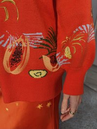 Suéter vermelho de malha com motifs de fruta, incluindo papaia e pepino, com punhos canelados e tecido texturizado.