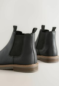Schwarze Leder-Chelsea-Stiefel verfügen über eine glatte Oberfläche, elastische Seitenpanels und Zuglaschen, mit einem braunen gestuften Absatz für zusätzlichen Kontrast.